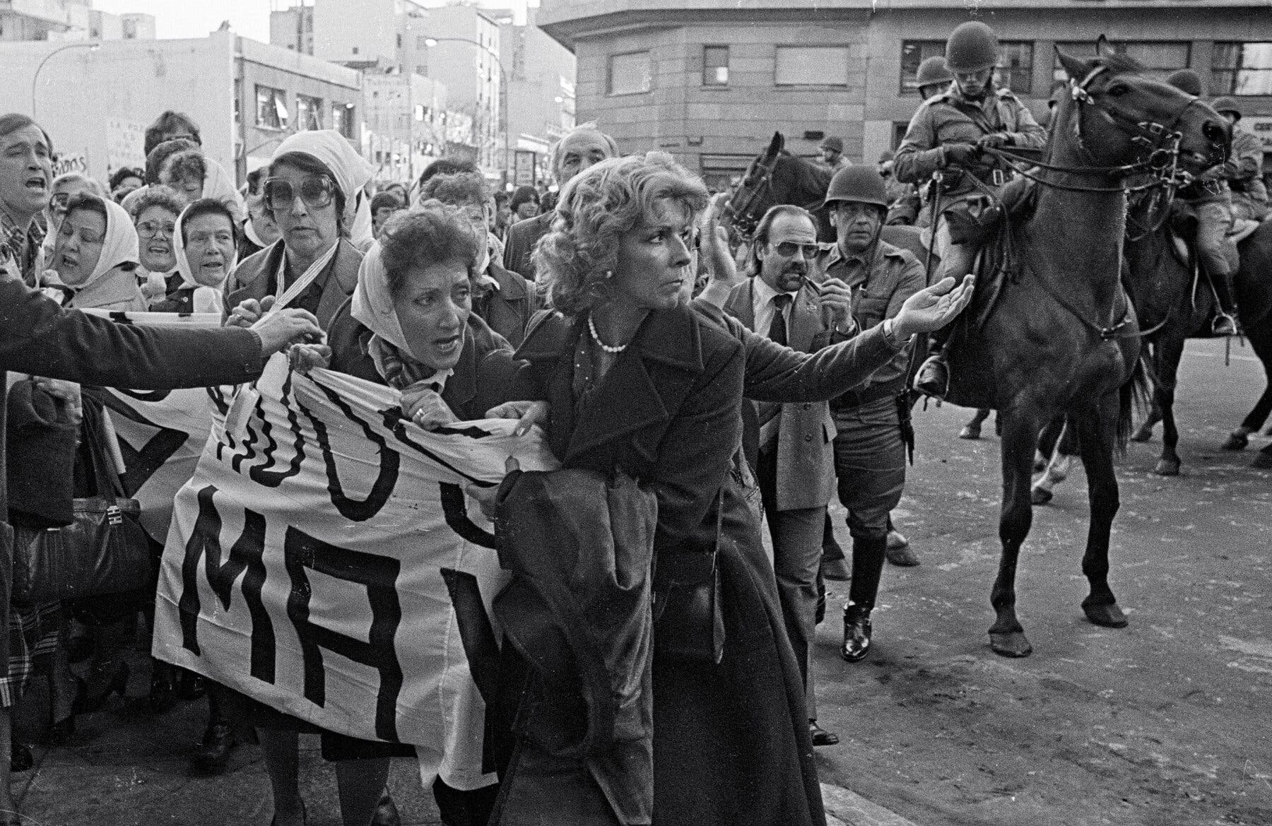 People holding a banner, as mounted police on horses stand nearby.