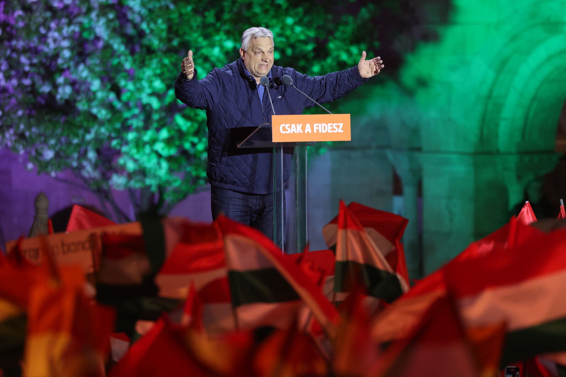 Viktor Orban speaks at a lectern with his arms outstretched.